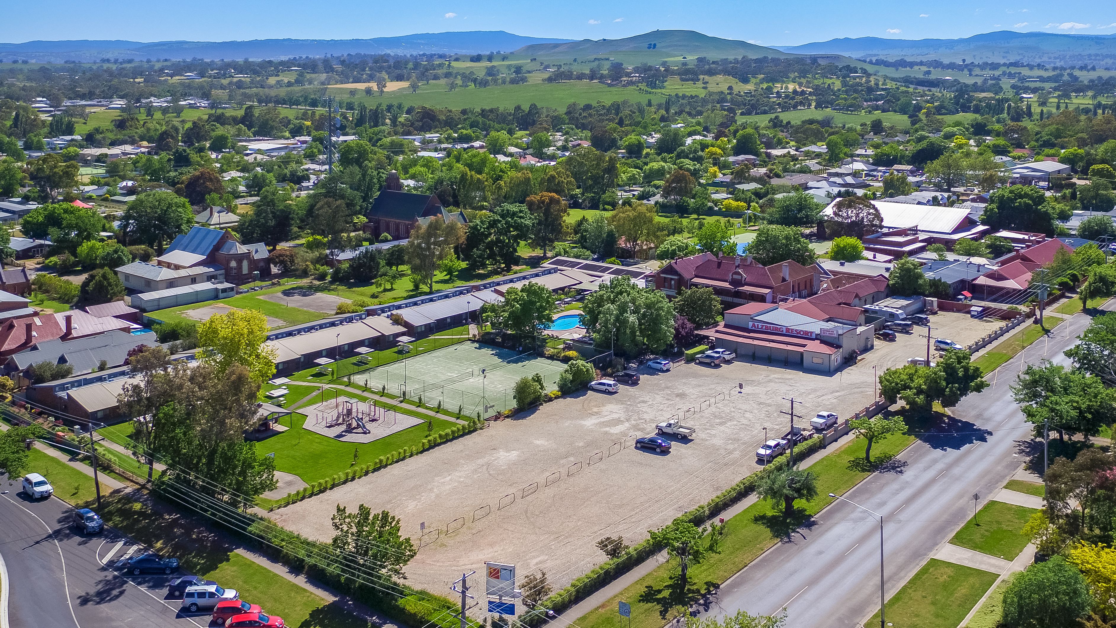 An aerial view of a resort with a swimming pool, tennis courts, and a parking lot.