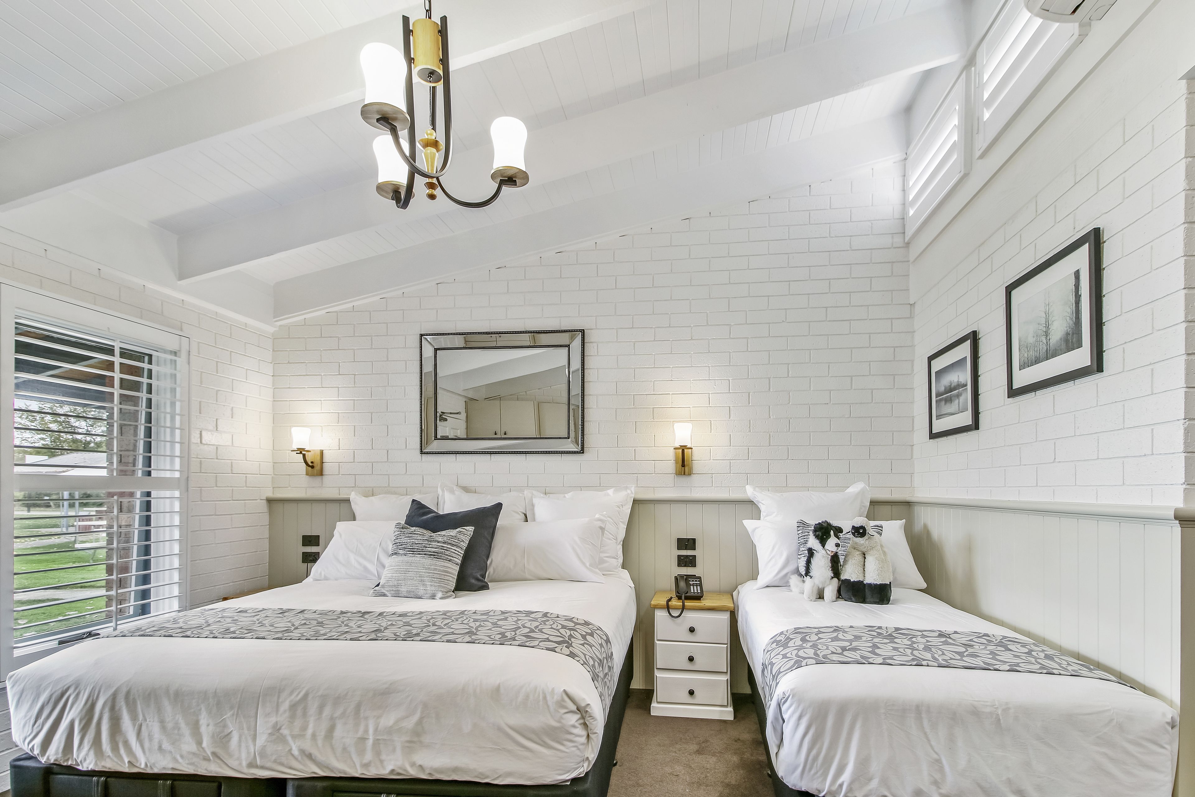 A bedroom with two beds, a chandelier, a mirror, and artwork on the walls.