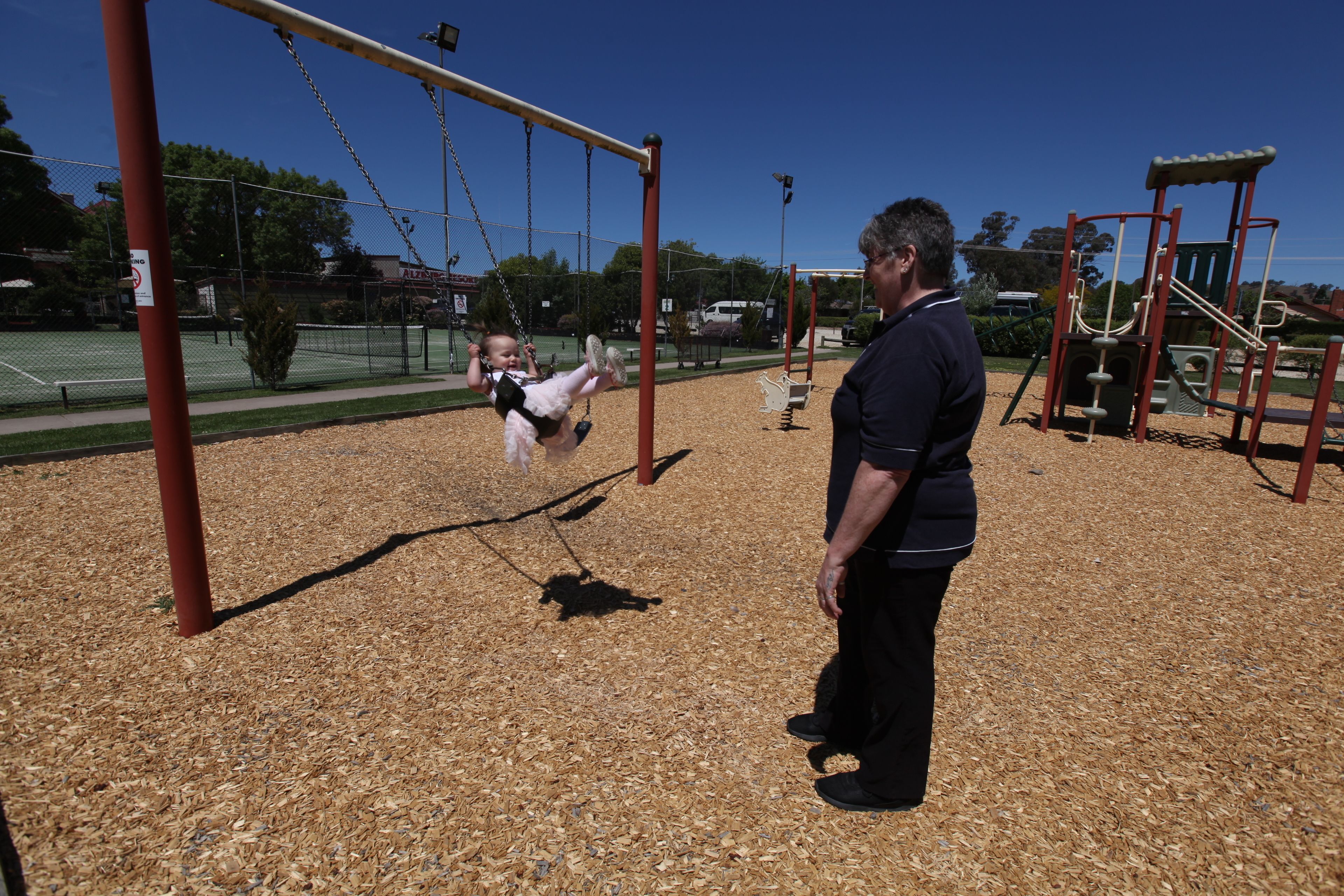 A playground with swings and a man standing nearby.
