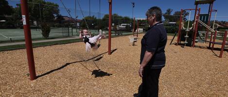 A playground with swings and a man standing nearby.