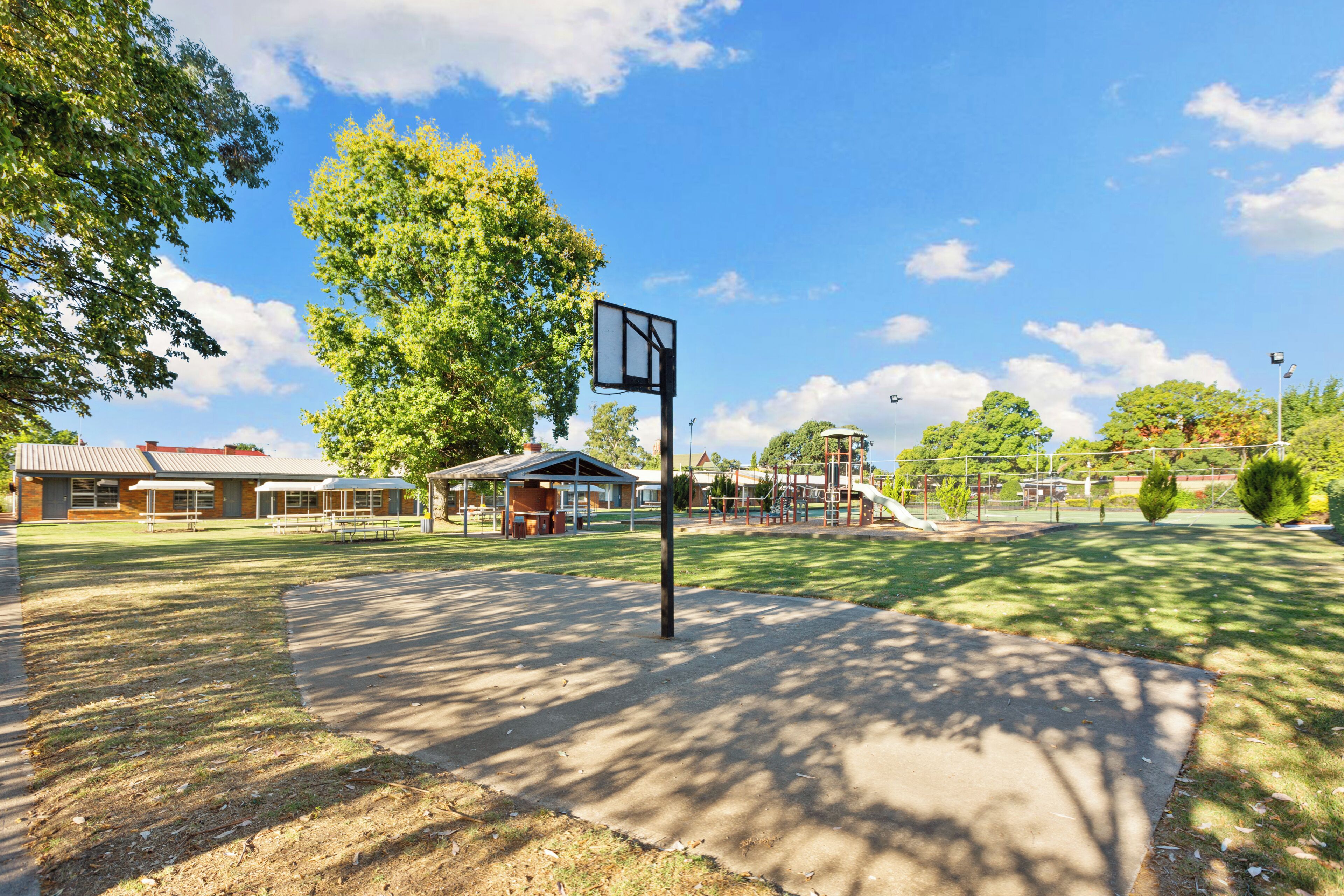 A basketball court with a hoop, picnic tables, and a playground in the background.