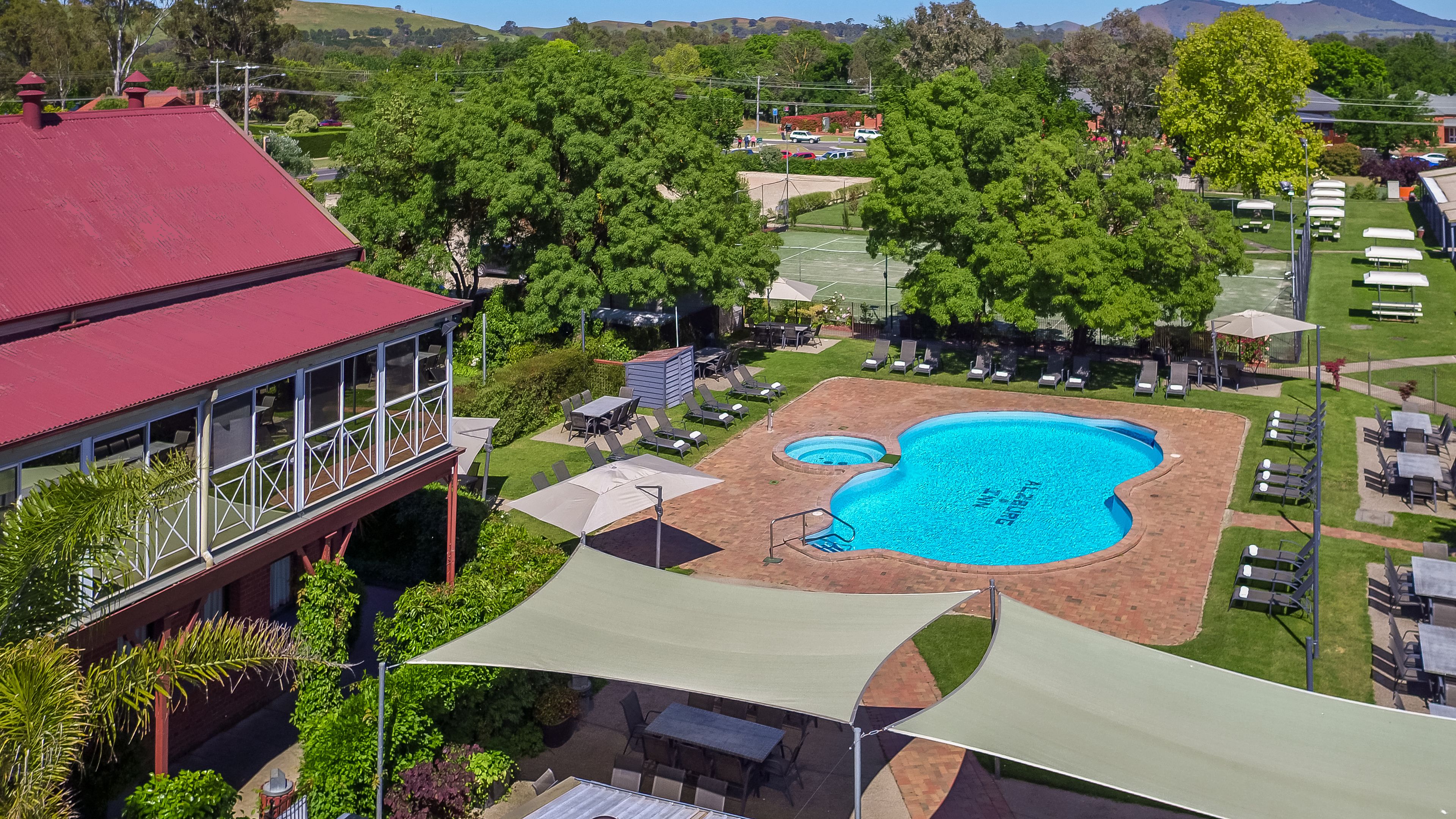 A pool area with a red-roofed building, outdoor seating, and a view of the surrounding landscape.