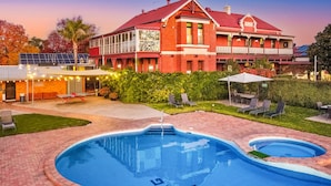 Une piscine au design original, entourée d’une pelouse bien entretenue et d’un grand bâtiment doté d’un toit rouge.