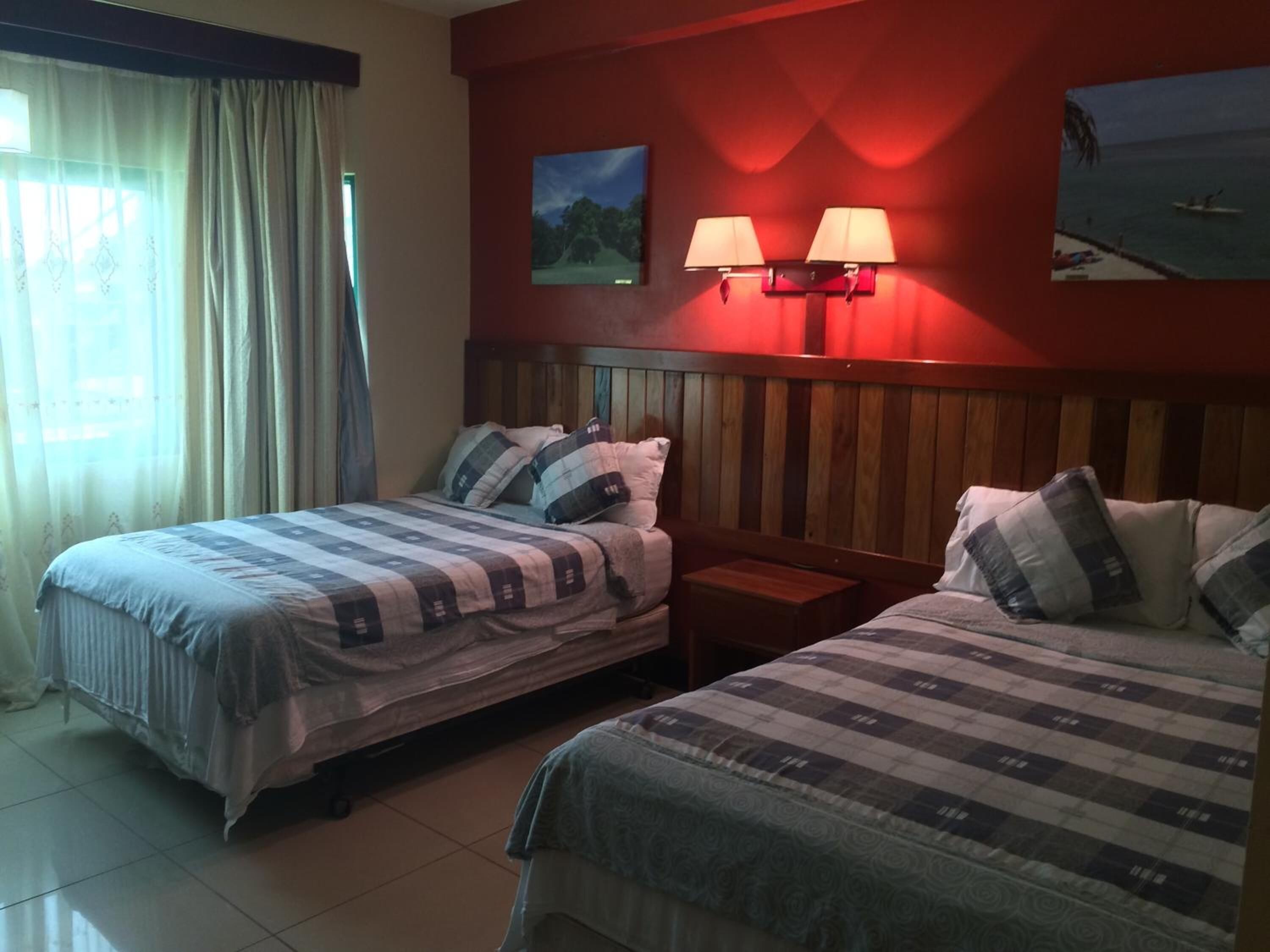 Une chambre d’hôtel avec deux lits, une table de chevet, une lampe fixée au mur et une vue sur la plage.
