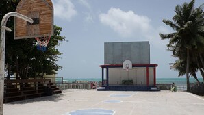 Een buitenbasketbalveld met een houten basketbalring, een betonnen constructie met een basketbalring, en uitzicht op de oceaan.