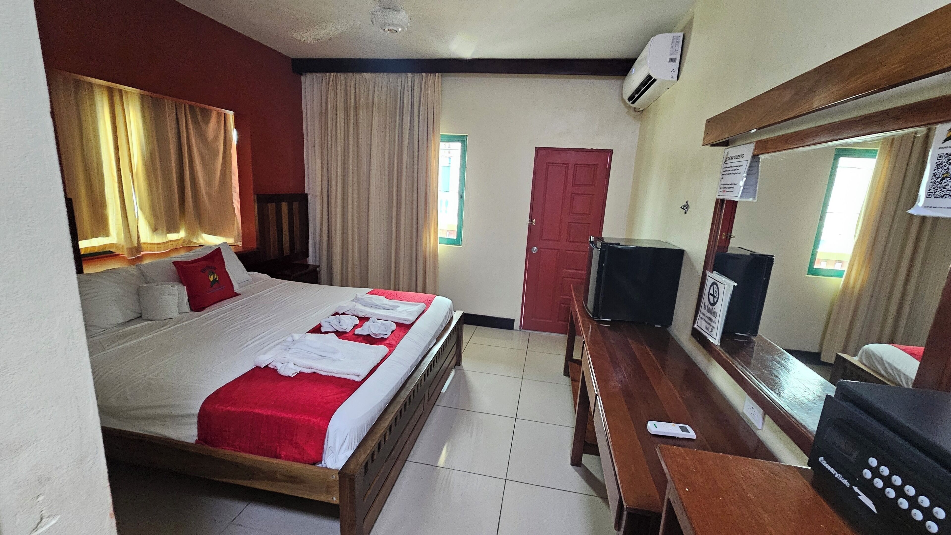 Una habitación de hotel con cama, escritorio, computadora, televisor y espejo.