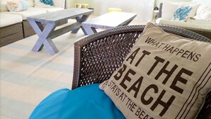 Een gezellig zithoekje met rieten meubels, een houten tafel en een kussen met tekst.