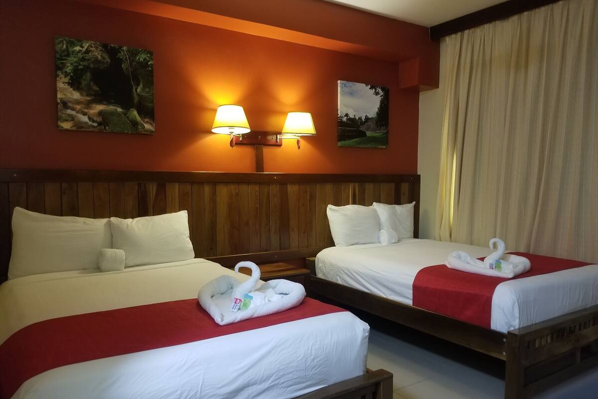 Habitación de hotel con dos camas, cabeceros de madera, ropa de cama blanca y dos lámparas fijadas a la pared.