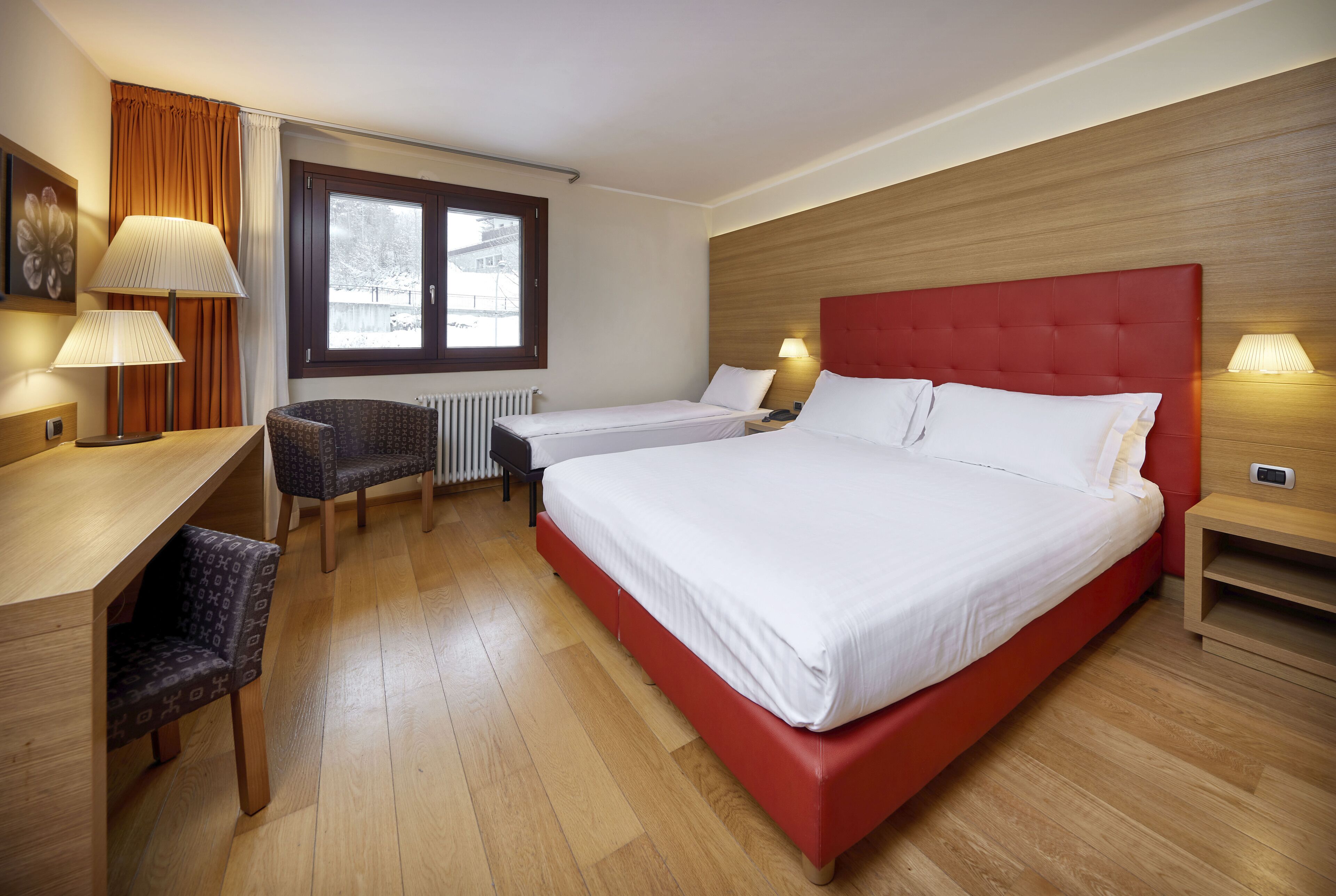 A hotel room with a large bed, a desk, a chair, and a window with curtains.