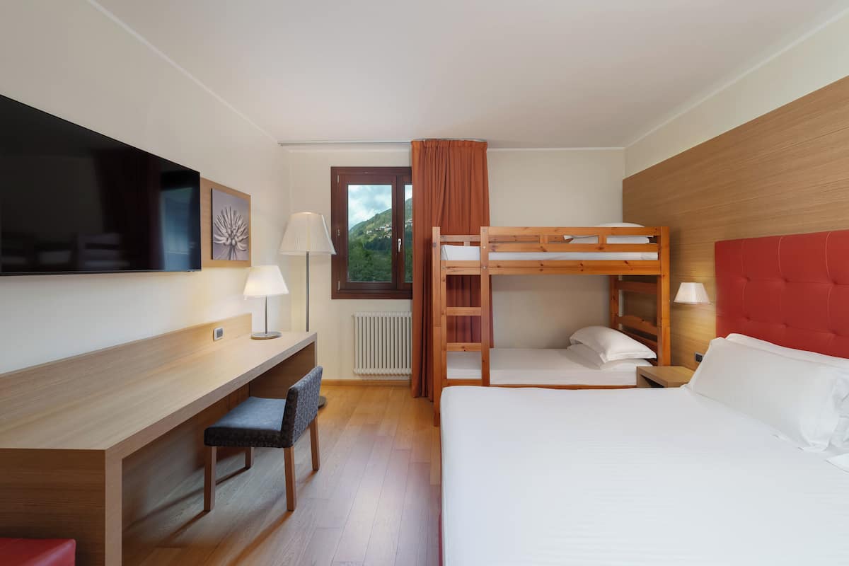 Une chambre d’hôtel avec un lit superposé, un bureau avec une chaise, une télévision et une fenêtre avec des rideaux.