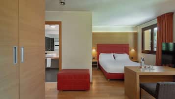 A hotel room with a wooden wardrobe, a red bed, a wooden desk, and a television.