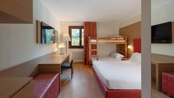 A hotel room with a bunk bed, a desk with a chair, a red bench, a television, and a window with curtains.