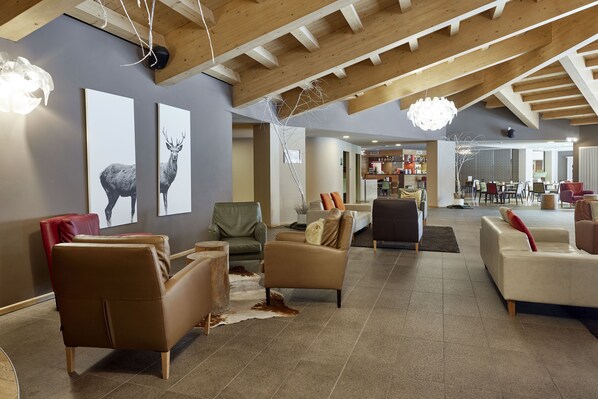 A spacious living area with leather sofas, a wooden ceiling, and artwork on the walls. - Blu Hotel Acquaseria (Ponte di Legno)