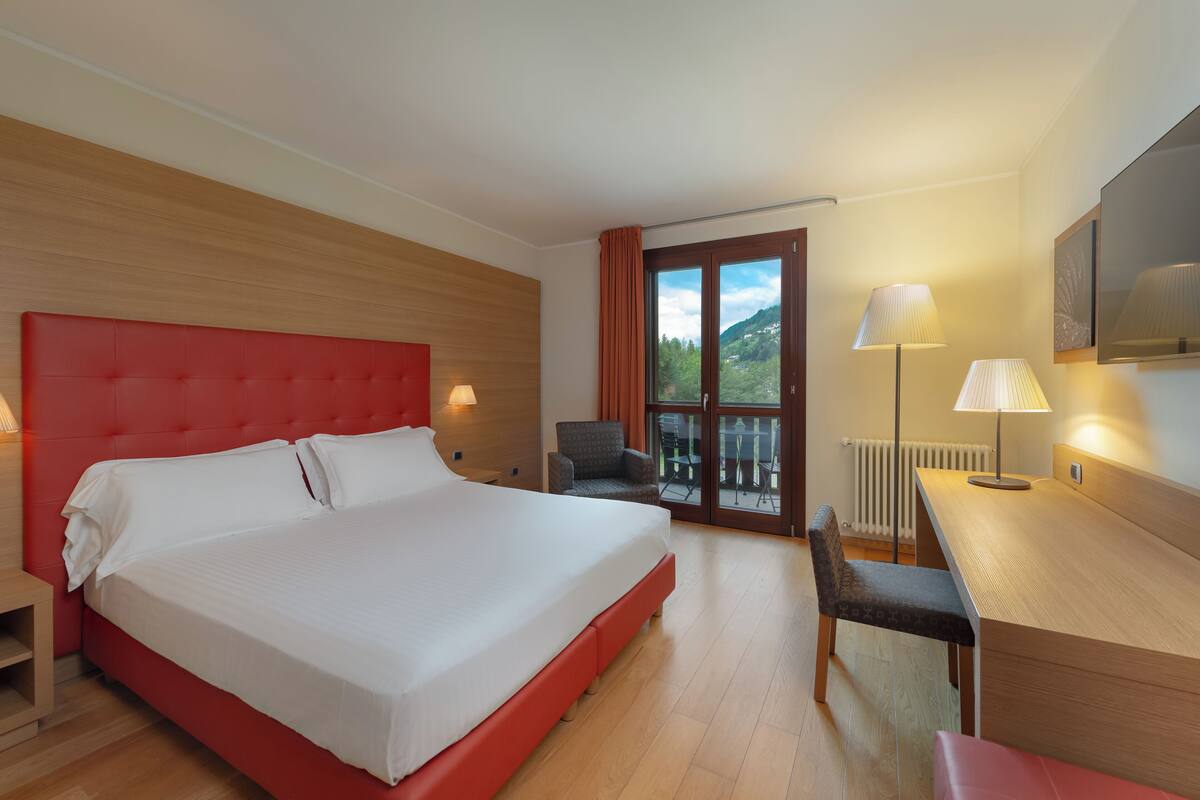 Une chambre d’hôtel avec un grand lit, un bureau, une chaise et une vue sur l’extérieur.