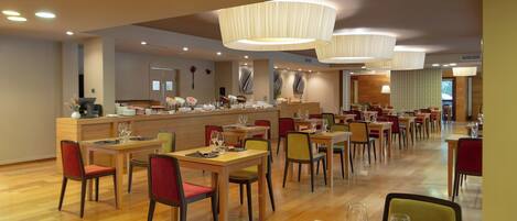 A modern restaurant with wooden tables and chairs, a buffet area, and pendant lighting.