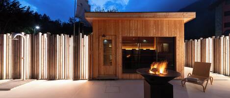 A modern wooden building with a fire feature in the center, a glass door entrance, and a wooden fence surrounding the area.