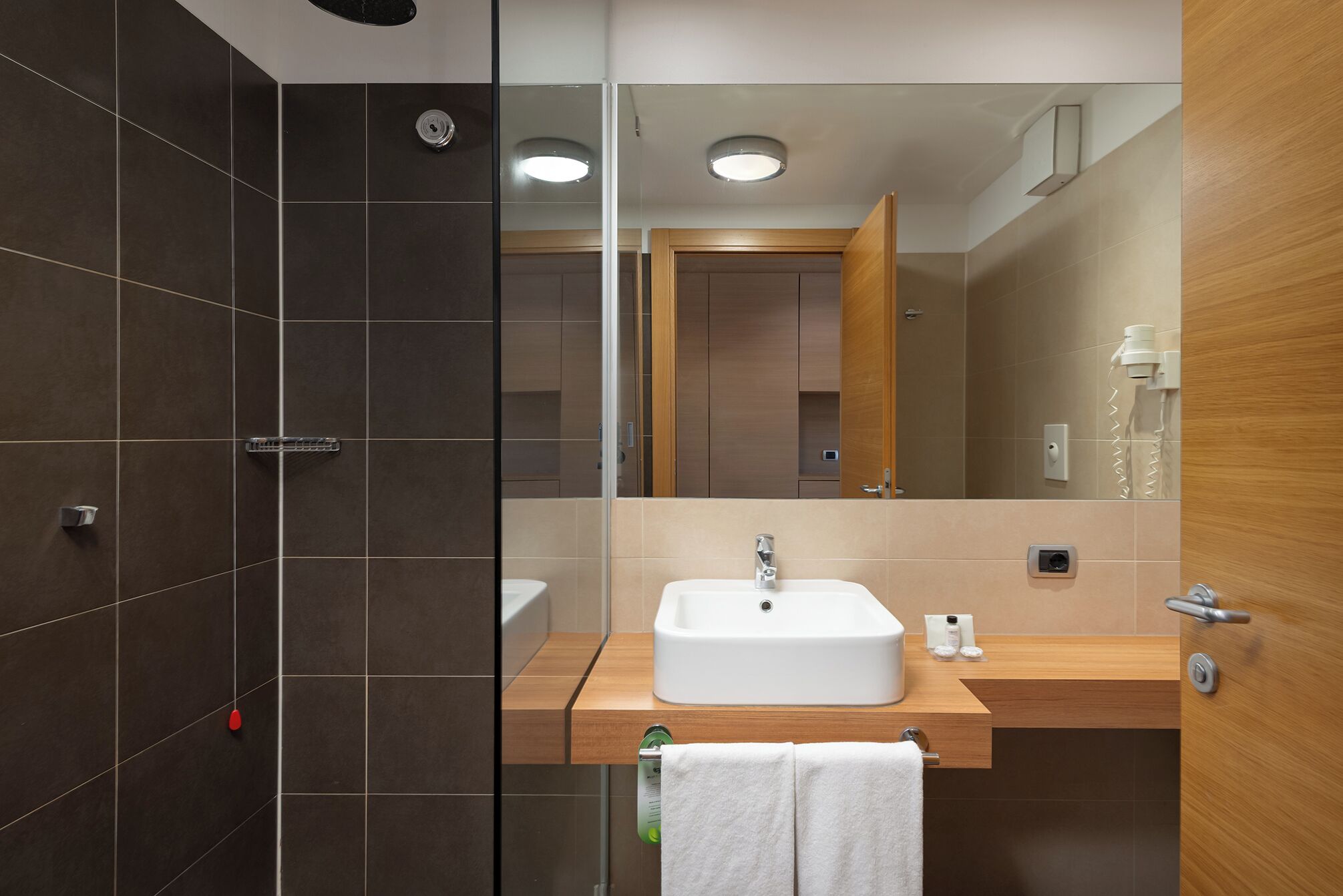Un baño moderno con un espejo grande, un lavamanos blanco y una zona de ducha.