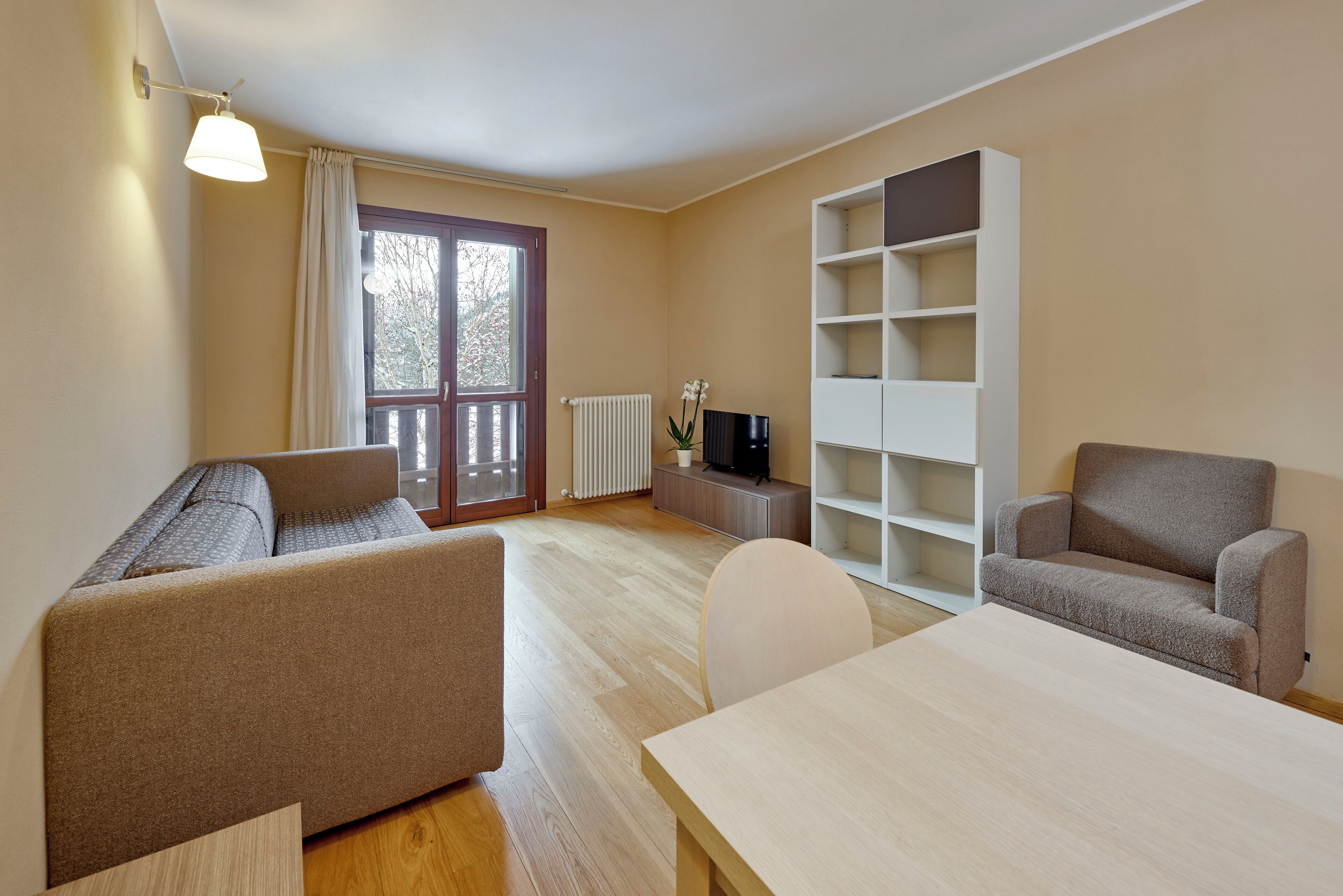 A modern living room with a sofa, a dining table, a TV, and a bookshelf.