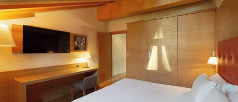 A modern hotel room with a large bed, a desk, a chair, a TV, and a wardrobe.