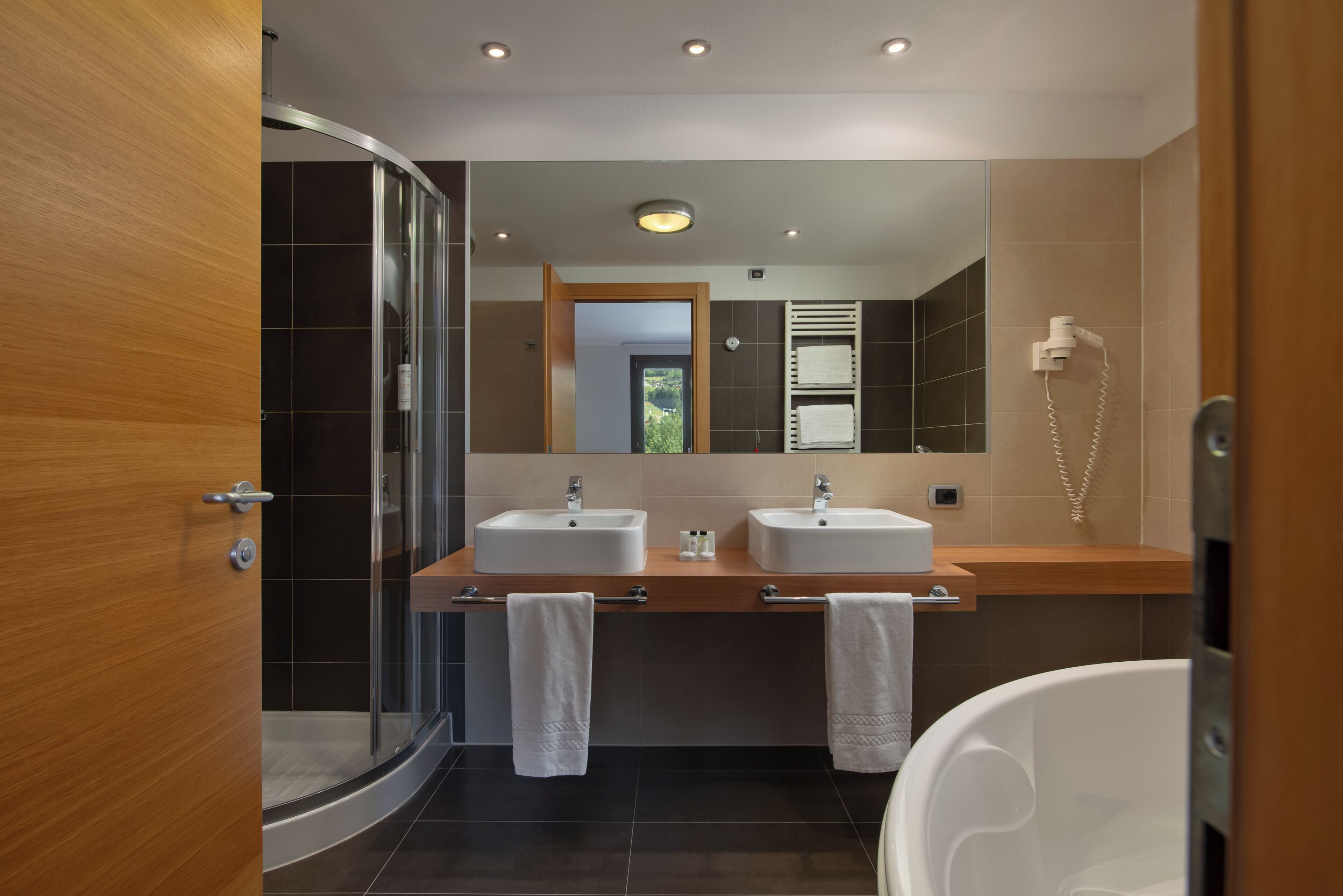 Ein modernes Badezimmer mit Duschabtrennung aus Glas, zwei Waschbecken, einem großen Spiegel und einer Toilette.