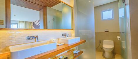 A modern bathroom with a wooden vanity, two sinks, a toilet, and a glass shower enclosure.