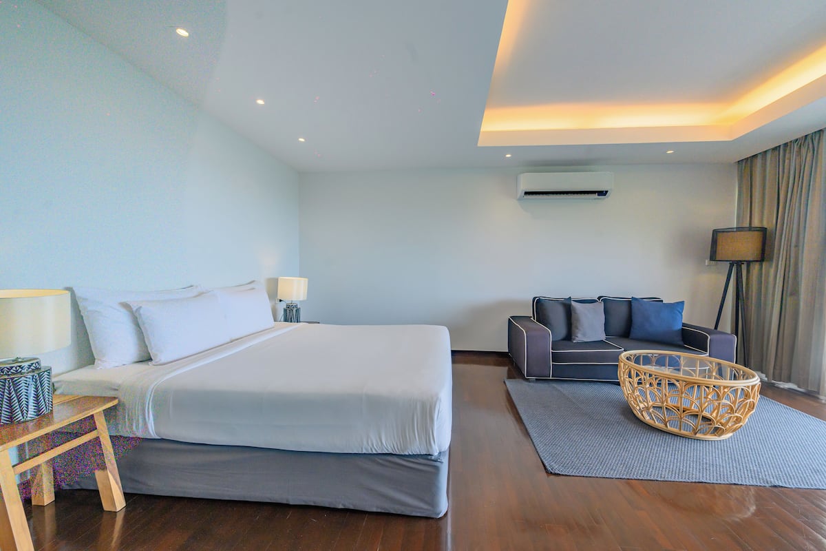 Una habitación de hotel moderna con una cama grande, un sofá, una mesita de mimbre y una lámpara.