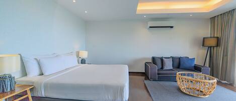 Una habitación de hotel moderna con una cama grande, un sofá, una mesita de mimbre y una lámpara.