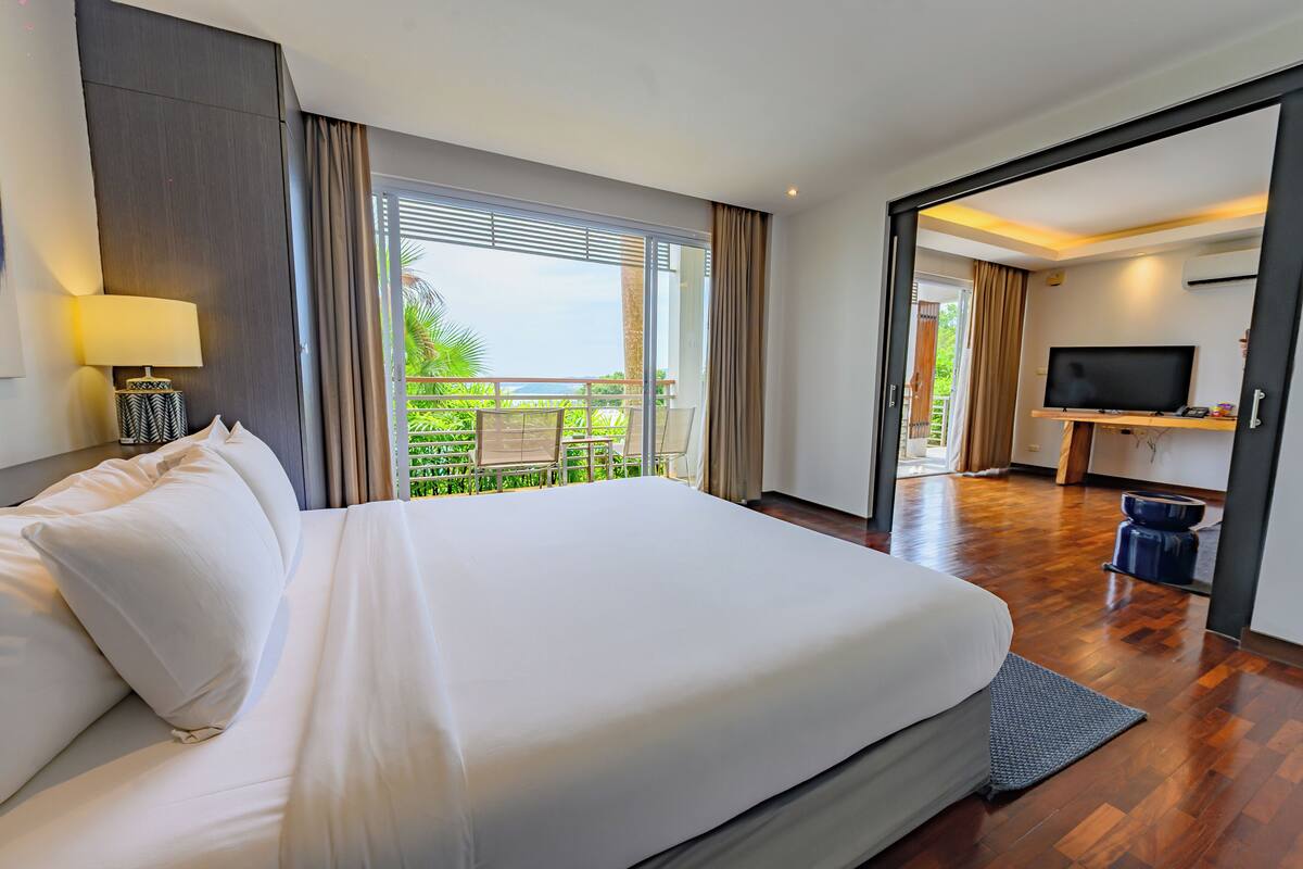 Habitación de hotel con una cama grande, televisión y balcón con vistas a zonas verdes.