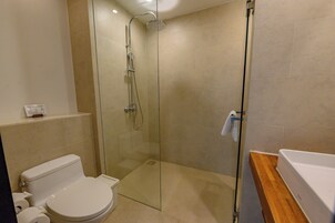 Un baño moderno con ducha de vidrio, inodoro blanco y tocador de madera.