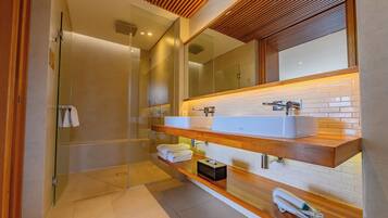 Un baño moderno con cabina de ducha de vidrio, tocador de madera con un lavamanos grande y un espejo sobre el tocador.
