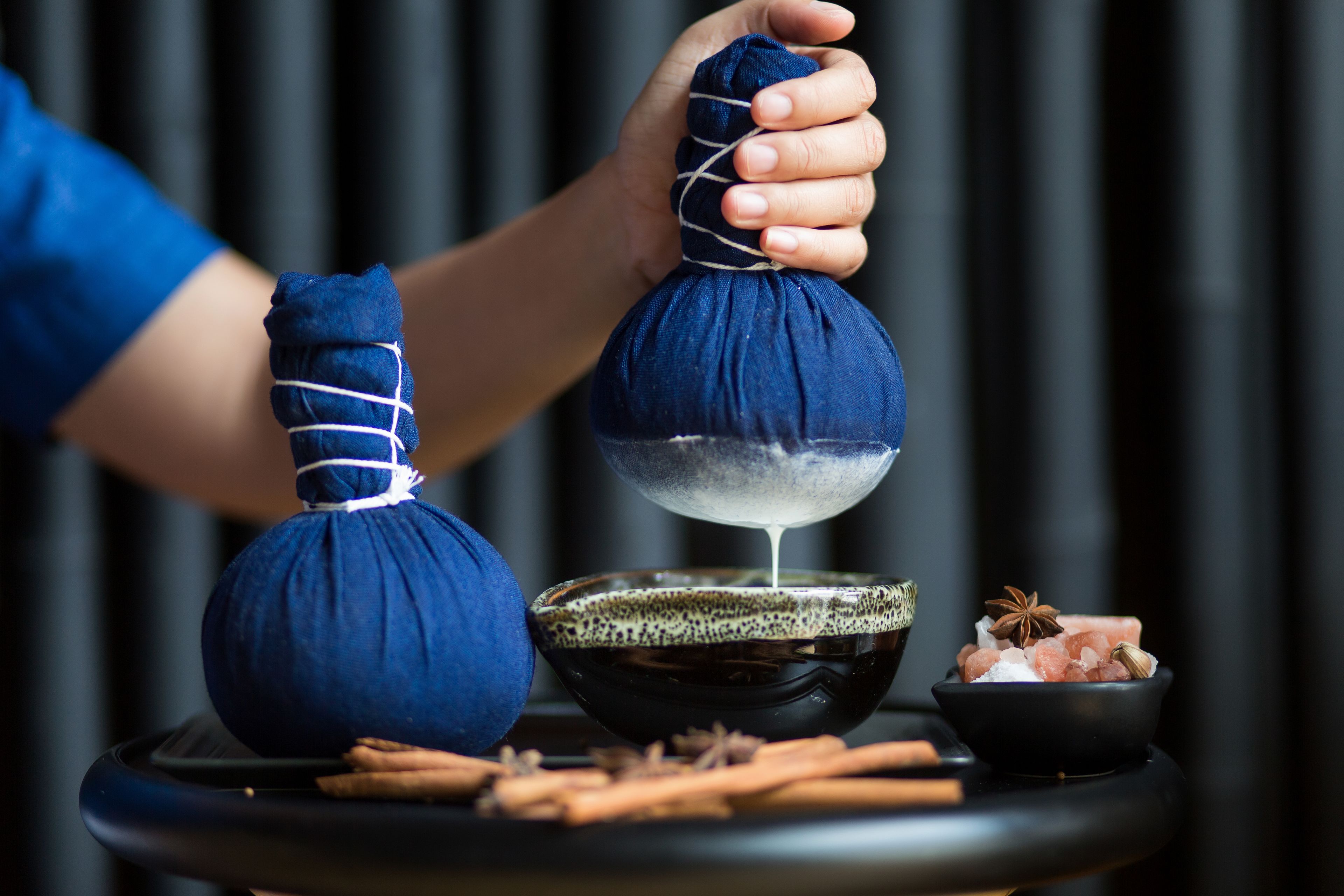 A person pouring a liquid from a blue bag into a bowl on a black tray.