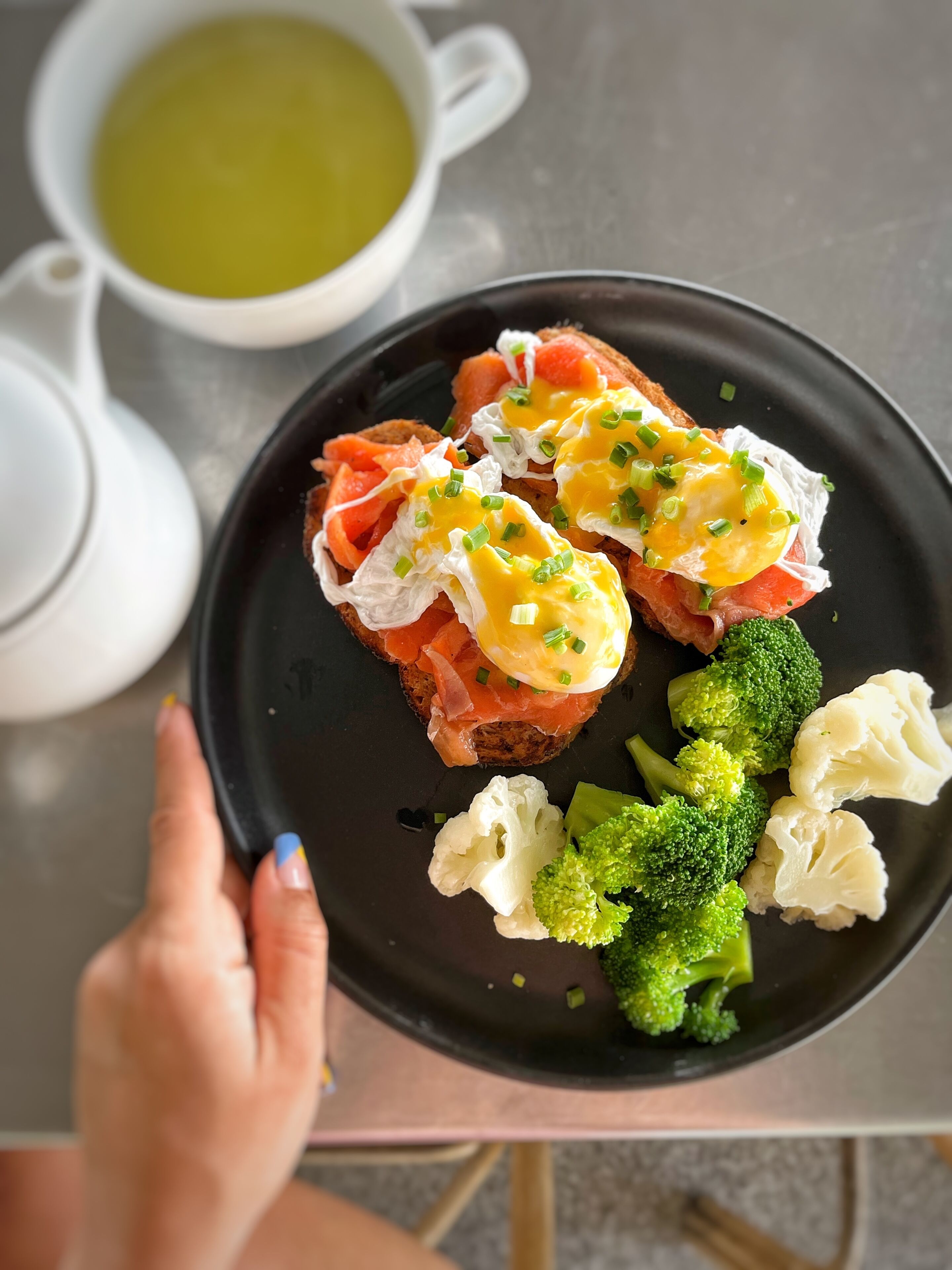 Un plato con alimentos como salmón ahumado, huevos y verduras, sostenido por una persona.