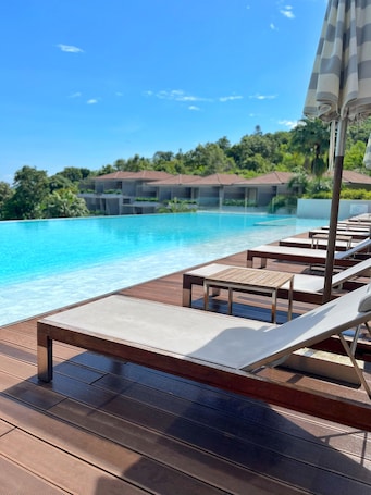 Una piscina al aire libre, sombrillas, sillones reclinables de piscina