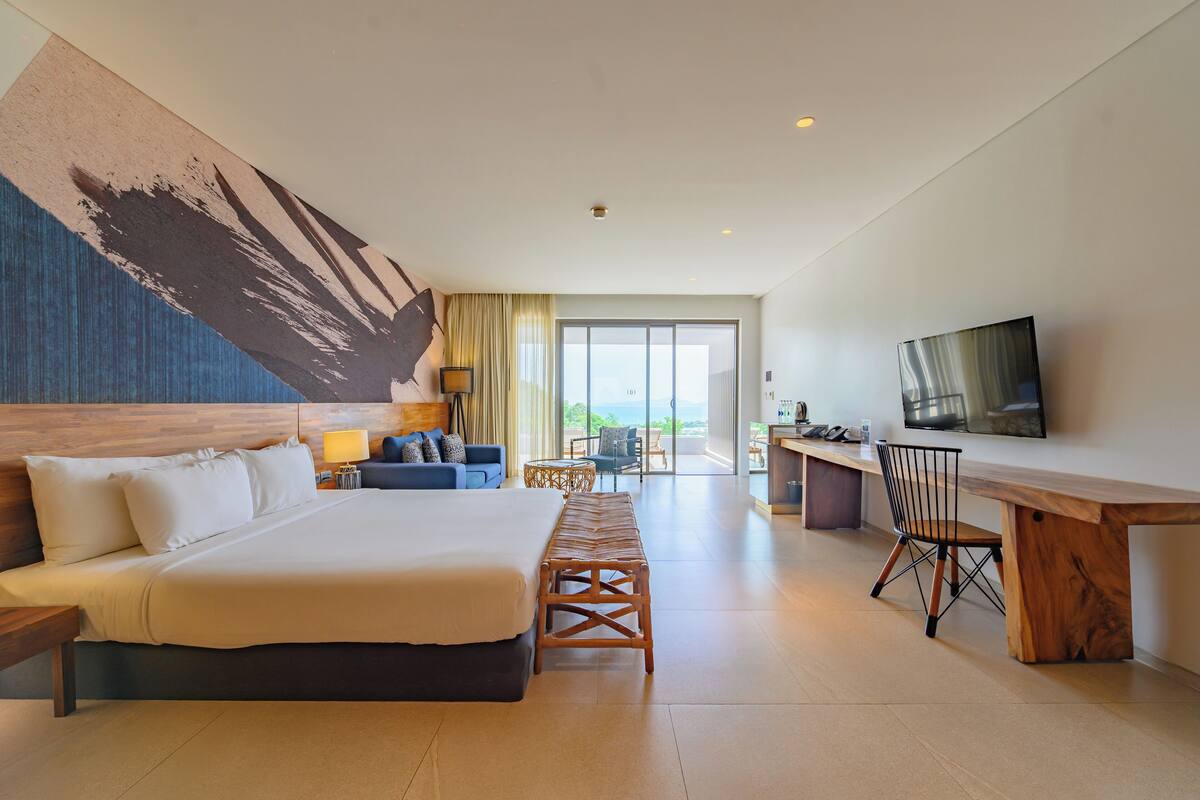 Habitación de hotel con una cama grande, un escritorio con silla, televisión y vistas al exterior.