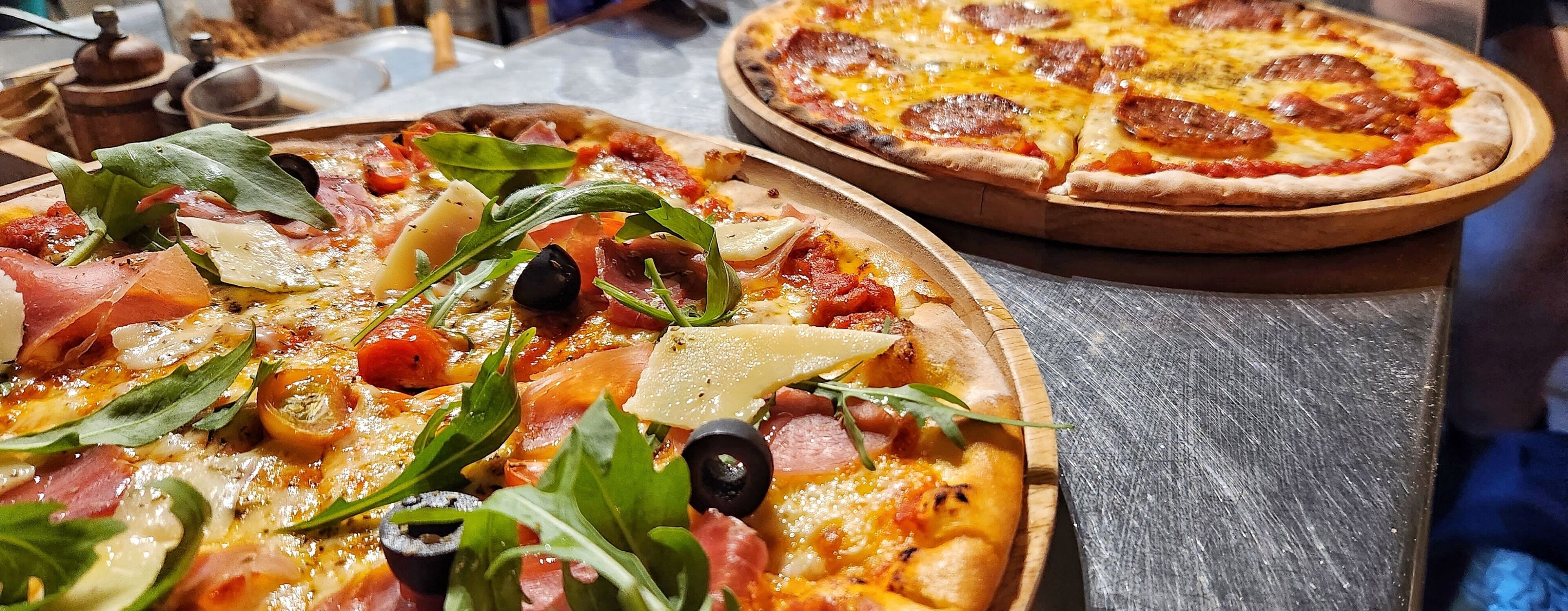 Zwei Pizzen mit unterschiedlichen Belägen auf einem Holzboden.