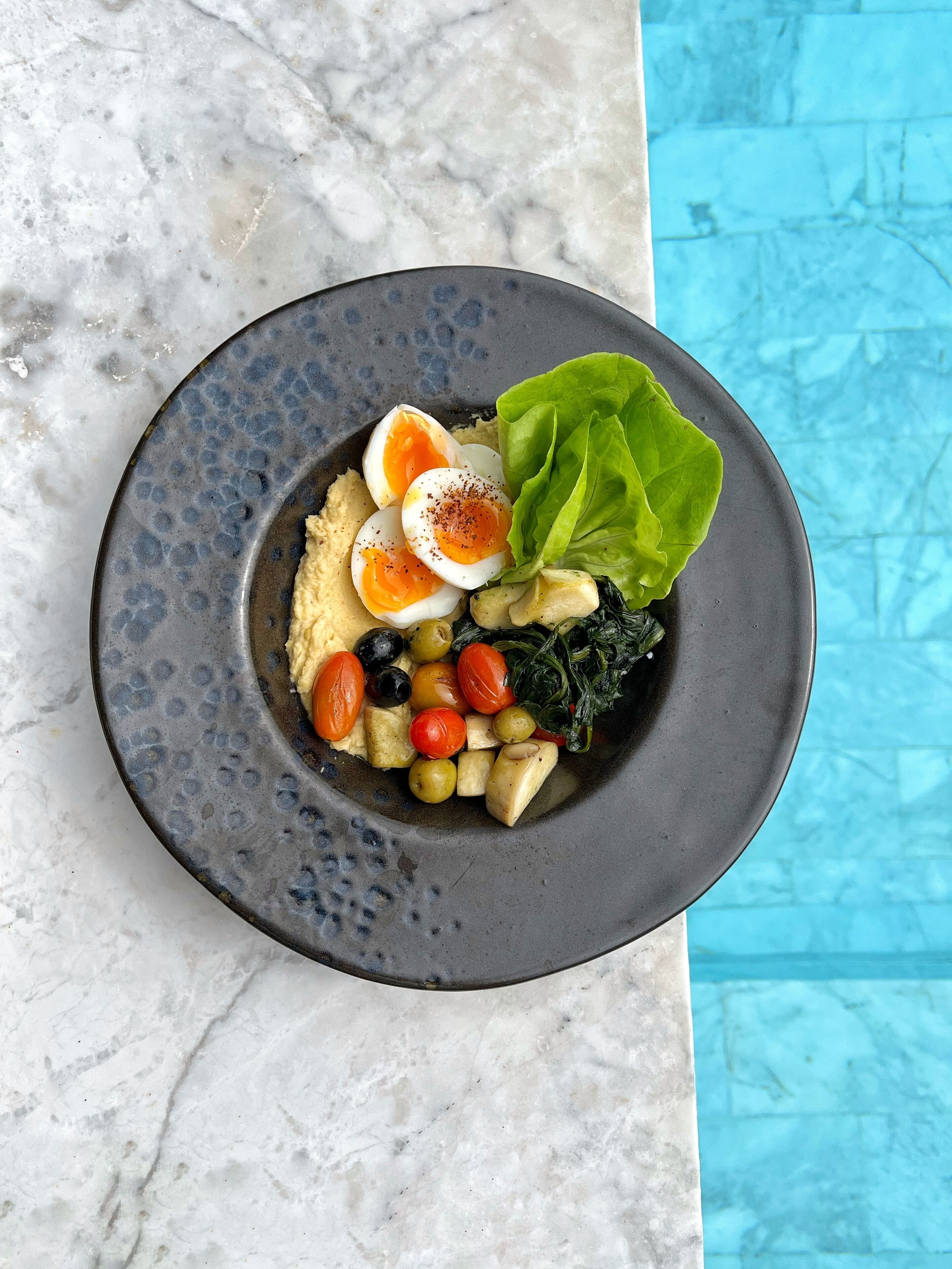 Un bol de nourriture contenant des œufs, des légumes verts et d’autres légumes, le tout présenté sur une assiette.