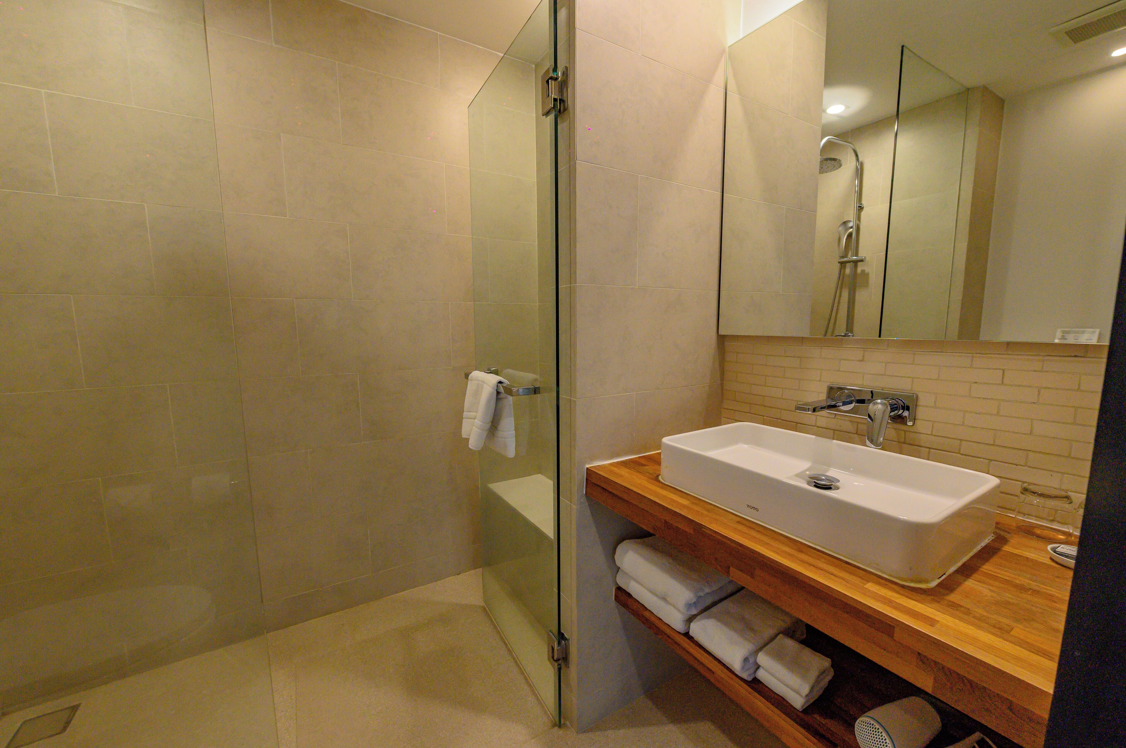 Un baño moderno con ducha envuelta en vidrio, tocador de madera con lavabo y espejo sobre el tocador.