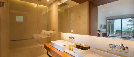 Un baño moderno con ducha envuelta en vidrio, un espejo grande y un mueble de tocador de madera con dos lavamanos.
