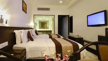 A hotel room with two beds, a TV, a desk, and a bathroom visible through a glass door.