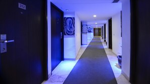 Et hotel med en blålig oplyst gang, nummererede døre og et tæppe på gulvet.