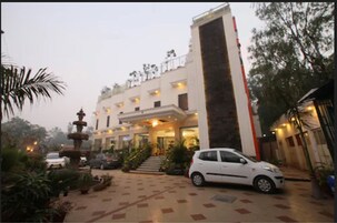 Un hotel con una fuente central, un coche blanco estacionado al frente y una entrada bien iluminada.