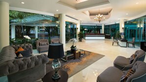 A spacious lobby with a modern design, featuring a seating area with sofas and armchairs, a reception desk, and a large glass window offering a view of the outdoors. - Delonix Hotel Karawang (Karawang)