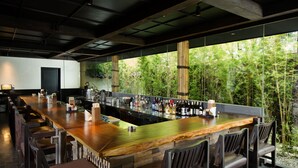 A bar area with a long counter, multiple seating options, and a view of greenery outside. - Delonix Hotel Karawang (Karawang)