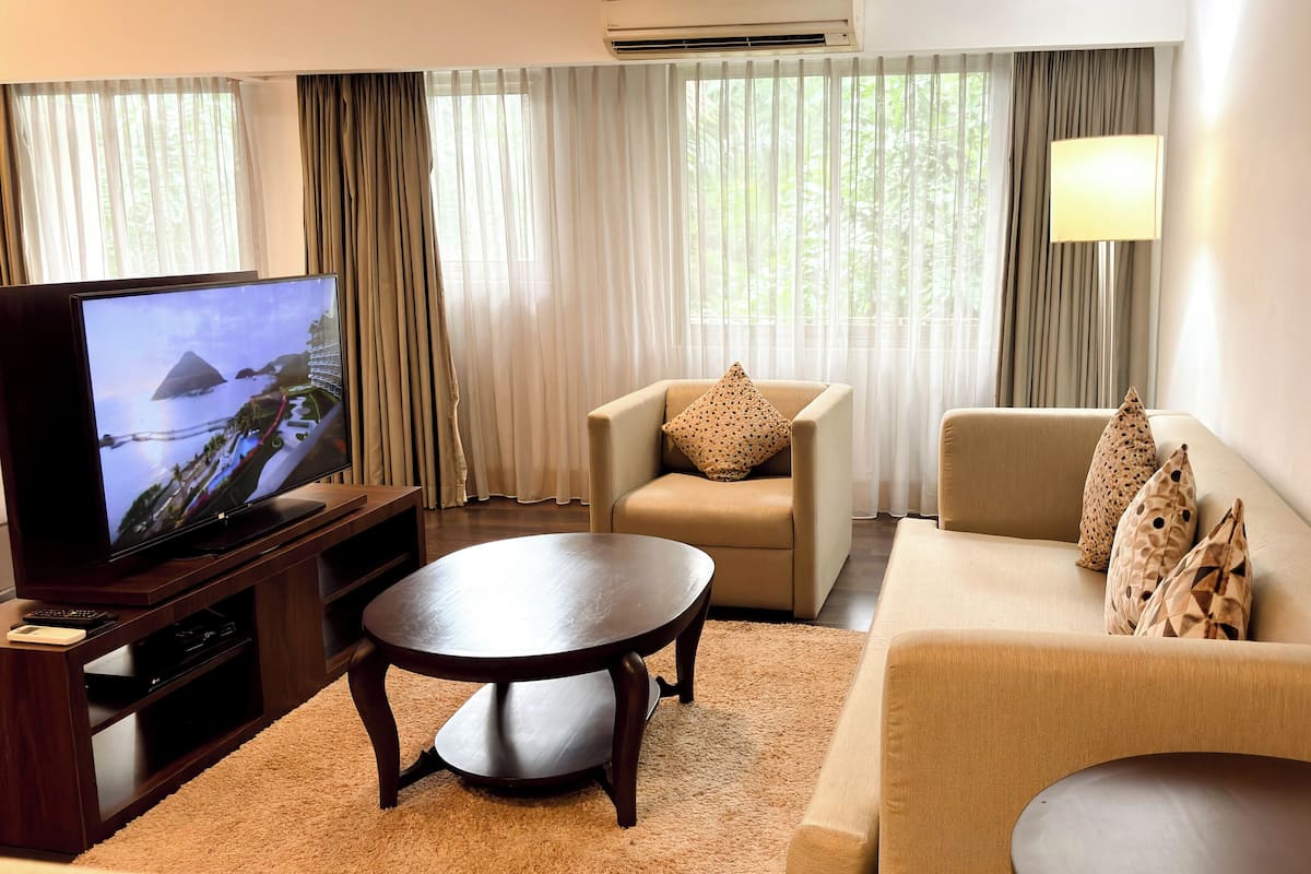 Uma sala de estar com televisão de tela plana, um sofá, uma poltrona, uma mesa de centro e um abajur.