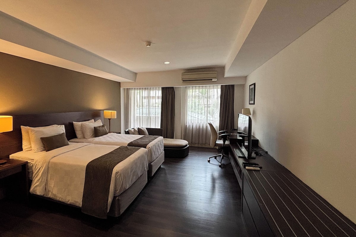 Quarto de hotel com duas camas, uma escrivaninha, uma cadeira e uma televisão.