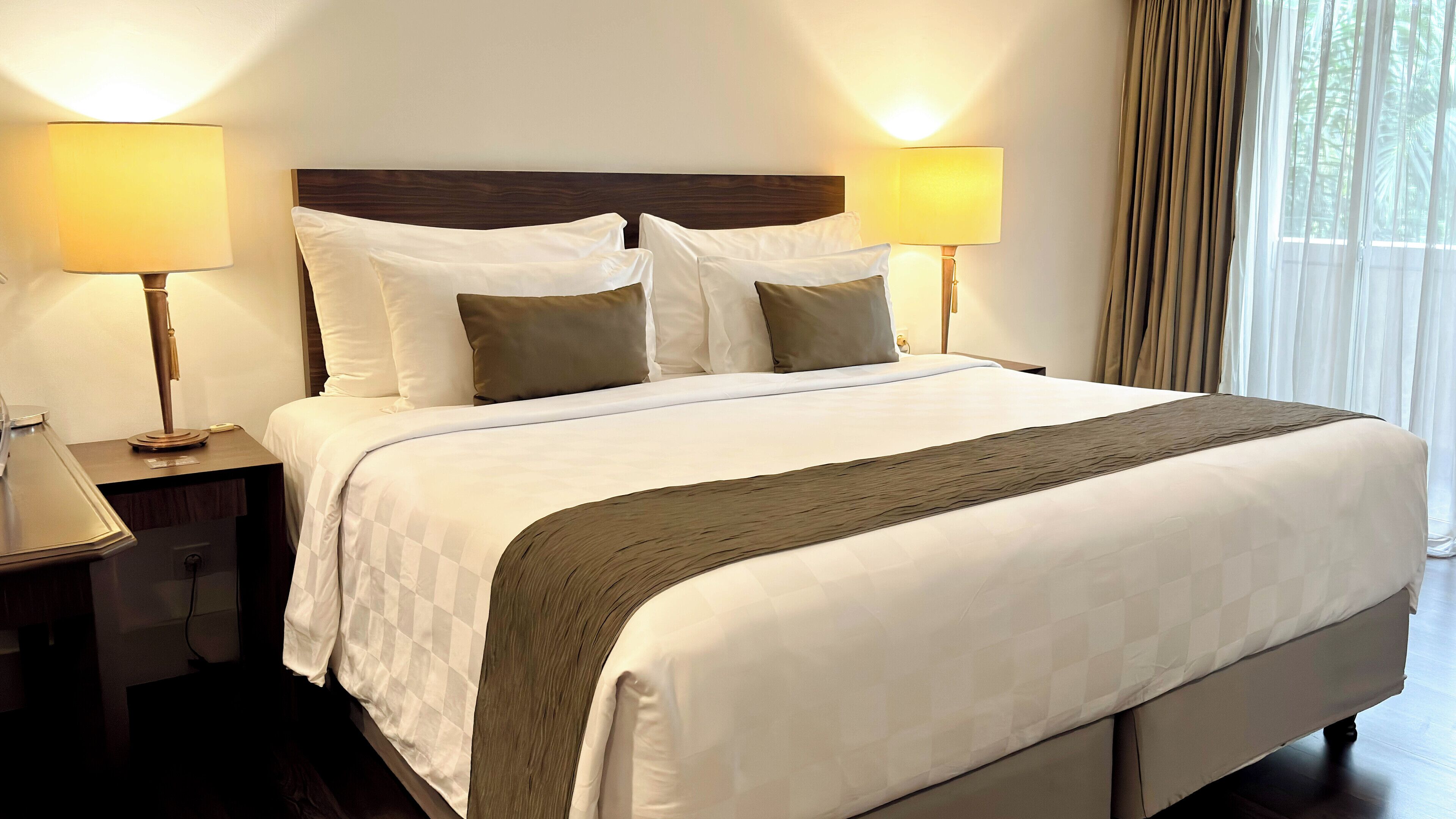 A neatly made bed with white and brown bedding, two bedside lamps, and a wooden headboard.