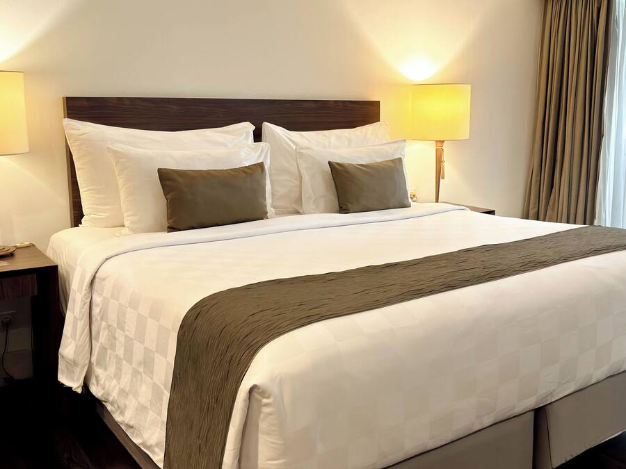 A neatly made bed with white and brown bedding, two bedside lamps, and a wooden headboard.