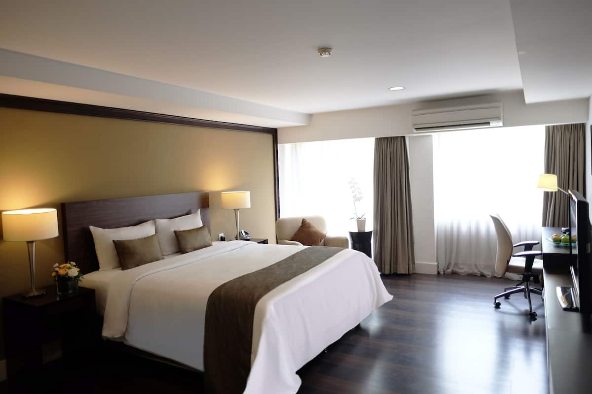 Quarto de hotel com cama grande, abajures, escrivaninha com cadeira e janela com cortinas.