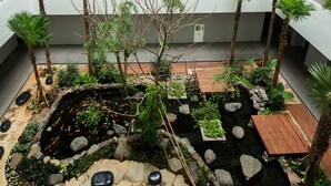 A multi-level atrium with a koi pond, stone pathways, and tropical plants. - Delonix Hotel Karawang (Karawang)