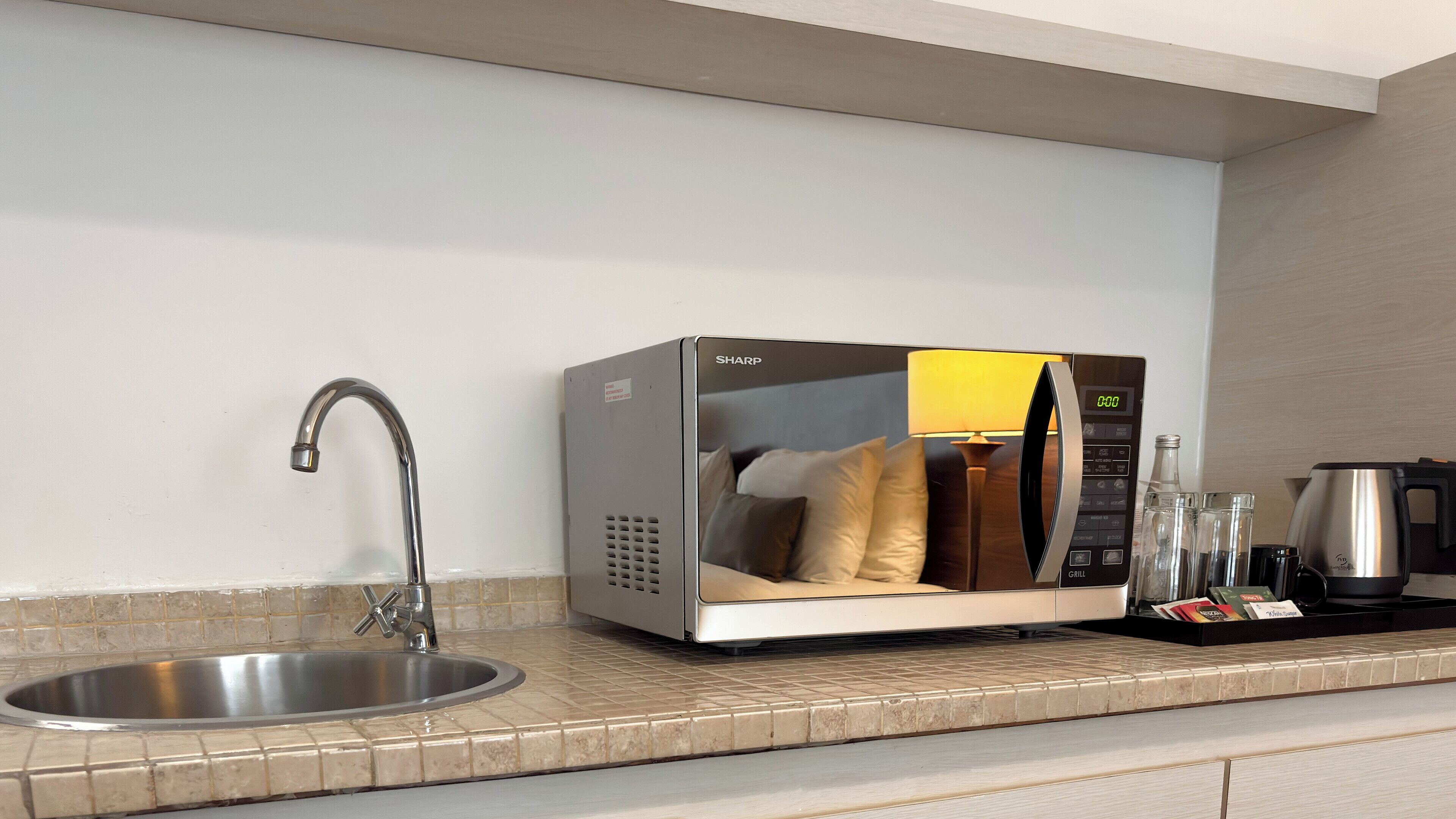 A modern kitchen with a built-in microwave, a stainless steel sink, and a kettle.